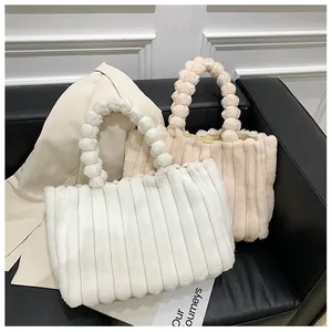 Détail de sacs cabas en peluche blanc et beige avec des anses à boules douces sur canapé