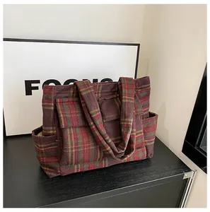 Detail of tartan wool tote bag showing red plaid texture and front flap pocket