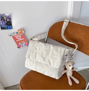 Detailweergave van beige gewatteerde postbode tas met hartpatroon en beerhanger