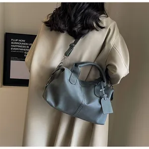 Detailansicht der mattgrau-blauen Boston-Tasche getragen über einem beigen Trenchcoat