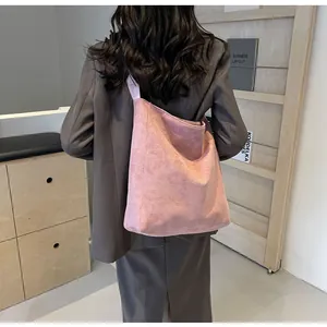 Detail of pink suede tote bag with wide shoulder strap worn by model in a modern setting