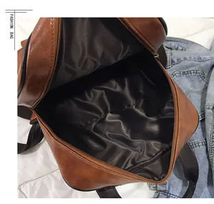 Detail view of the brown leather backpack showing a wide zip opening and smooth black lining