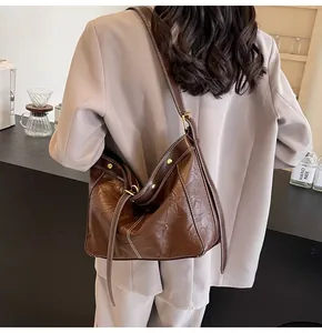 Detail of dark brown pleated leather shoulder bag with white stitching and gold rivets
