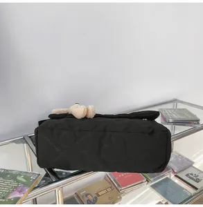 Detail van zwarte gewatteerde crossbodytas met hartjespatroon en pluchen beerhanger