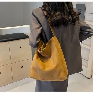 Close-up of a large camel suede tote bag with a wide shoulder strap worn by a model