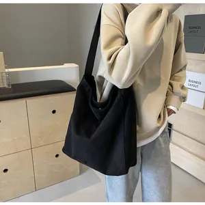 Hobo style large black canvas tote bag with wide shoulder strap worn on casual outfit