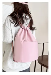 Rear view of a light pink nylon drawstring backpack with large front pocket on a model