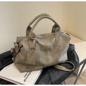 Nahaufnahme der taupefarbenen Boston-Tasche aus mattem Leder auf einer schwarzen Jacke
