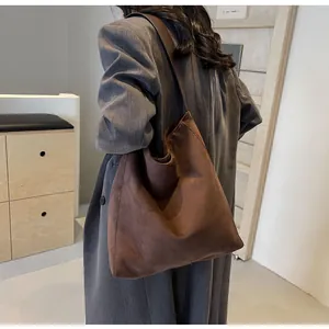 Model wearing dark brown oversized suede tote bag with wide strap in minimalist interior