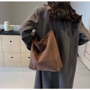 Detail einer großen braunen Hobo-Tasche mit breitem Schultergurt über einem grauen Mantel