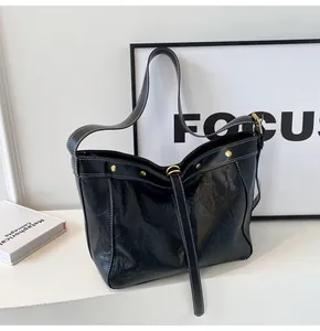 Detail of black faux leather tote bag with white stitching and gold rivet accents