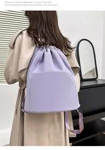 Back view of a light purple nylon drawstring backpack worn over a khaki trench coat