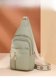 Detail of light green pebble leather chest bag with gold zippers and patterned strap