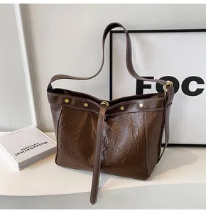 Detail of dark brown pleated leather tote bag featuring gold rivets and vintage texture