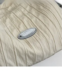 Détail macro du tissu en nylon plissé beige avec écusson logo en caoutchouc sur le sac