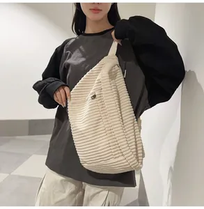 Model wearing a large cream corduroy crescent crossbody bag with black zipper detail