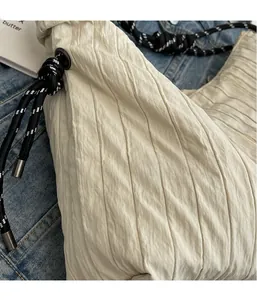 Détail du tissu plissé beige avec bandoulière en corde tressée noire et blanche