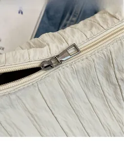 Gros plan sur la texture du tissu plissé beige et le détail du zip en métal argenté