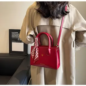 Detail der roten Brauthandtasche mit goldenem Herzakzent und kariertem Seidenschal-Accessoire