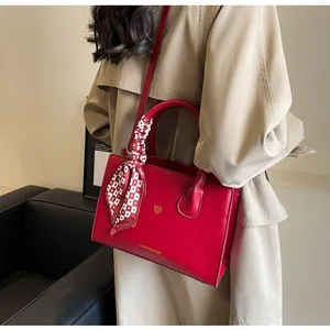 Detail der roten Brauthandtasche mit goldenem Herzlogo und dekorativem Karo-Halstuch