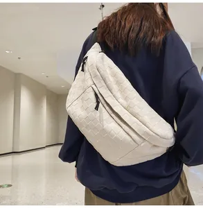 Detail of cream crossbody bag with checkerboard texture worn by model in a corridor