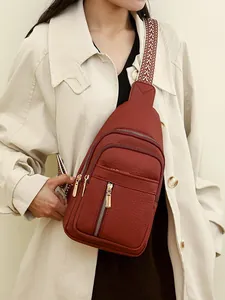 Red-brown pebble leather chest bag with woven strap shown on a model in trench coat