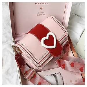 Borsa a tracolla rosa e rossa con fibbia a cuore in una confezione regalo su panno bianco