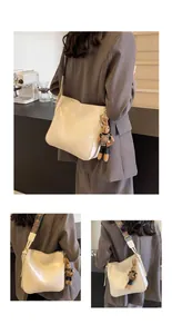 Detail van beige schoudertas met geometrische brede riem en schattige konijn-hanger
