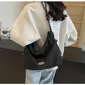 Détail du sac plissé noir avec bandoulière tissée et plaque de logo en métal brillant