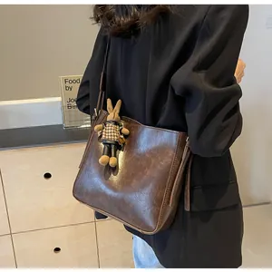 Detail van donkerbruine leren shopper met decoratieve rits en schattige konijnenhanger