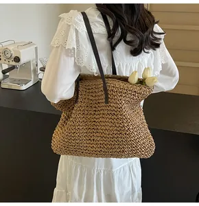 Detalle del bolso tote de paja tejida con correas marrones sobre un vestido de encaje
