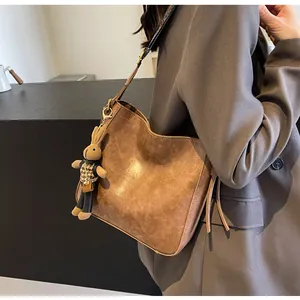 Detail van een bruine leren emmertas met een schattige konijnenhanger op een blazer
