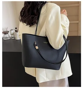Detailed close-up of matte black leather tote bag with gold metal hardware on model