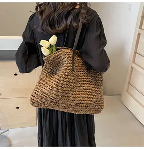 Detalle de un bolso tote grande de paja trenzada marrón con asas de cuero y tulipanes
