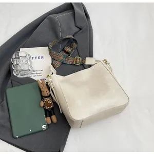 Detailoverzicht van beige emmertas met kleurrijke riem en schattige konijnenhanger