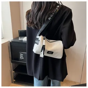 Detail of white cross-body pillow bag with wide branded letter strap and leather texture