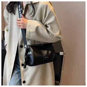 Detail of black leather crossbody pillow bag with wide branded strap on a model
