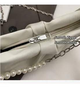 Close-up of smooth metal zipper and pearl chain detail on cream pleated cloud bag