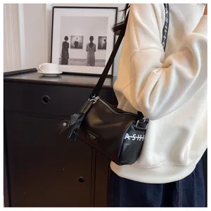 Close-up of black leather cylinder bag featuring white fashion lettering and wide strap