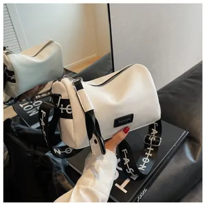 Detail of white pebbled leather pillow bag featuring black fashion logo and wide strap