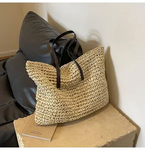Detalle del bolso tote de paja tejido a mano con asas de cuero marrón en base