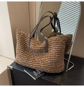 Detalle de bolso tote de paja tejida con asas largas de cuero marrón oscuro en mesa