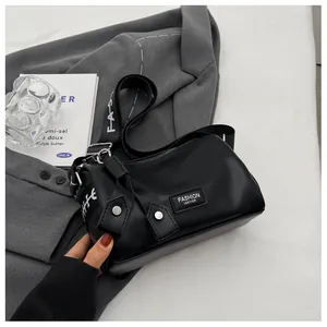 Close-up of black lychee texture crossbody bag with wide white letter print strap on a grey blazer