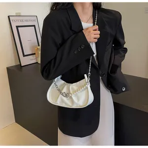 Detail of white pleated cloud bag featuring decorative pearls and fine metal chain strap