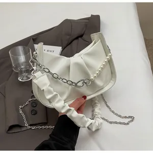 Detail of white pleated cloud bag with pearl and silver metal chain on a brown blazer