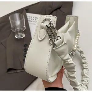 Detail of white pleated cloud bag showing silver hardware and pearl strap attachment
