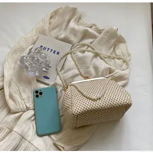 Detailed macro view of woven straw clutch bag with pearl chain and golden kiss-lock closure
