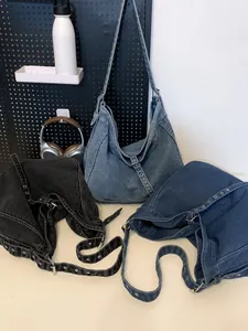Three oversized denim hobo bags in black and blue colors with metallic eyelet straps