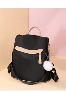 Détail du sac à dos antivol noir avec garniture en cuir beige et pompon blanc doux