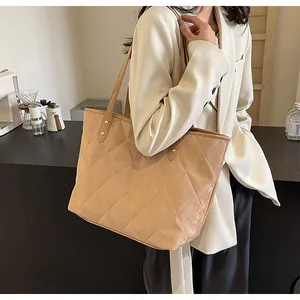 Detail of quilted tote bag in beige with metal rivets and shoulder straps worn by model